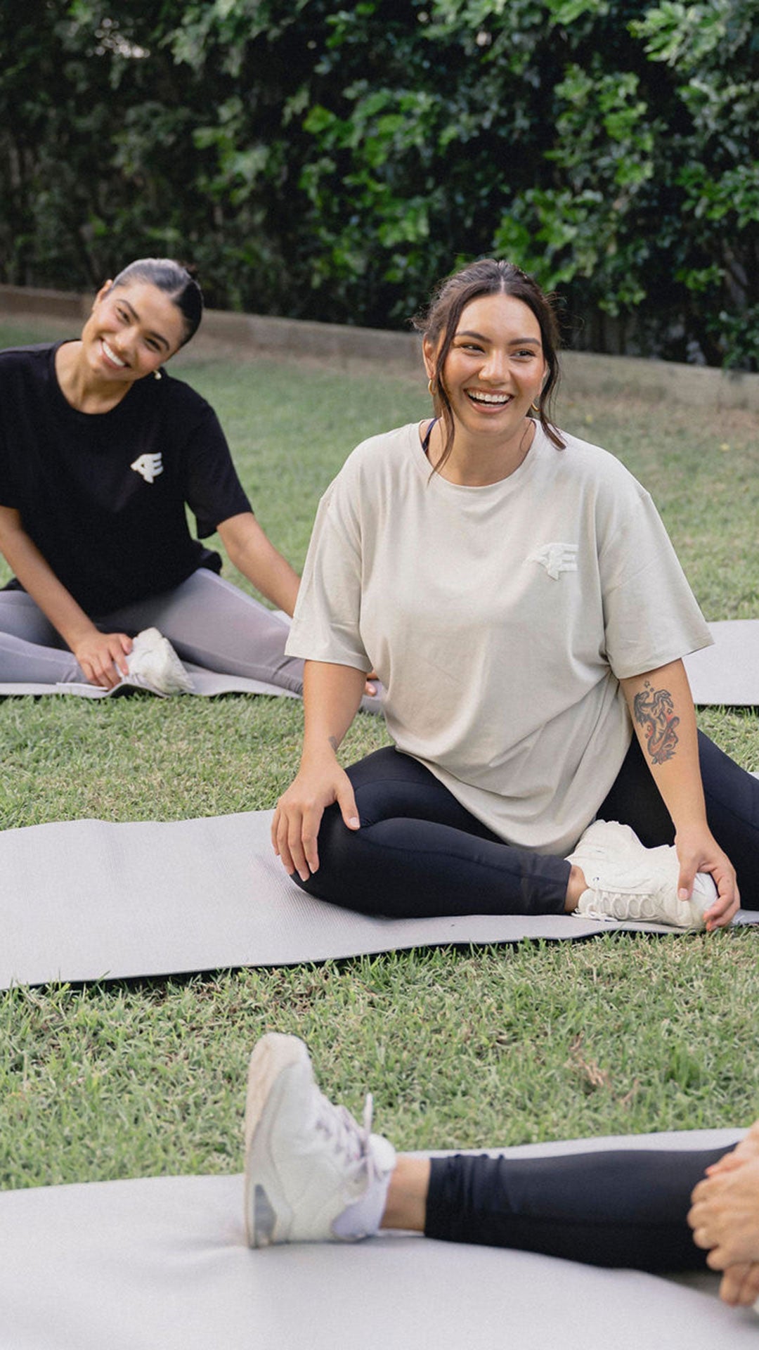 A group of women sitting on yoga mats outside, enjoying a relaxing moment together.