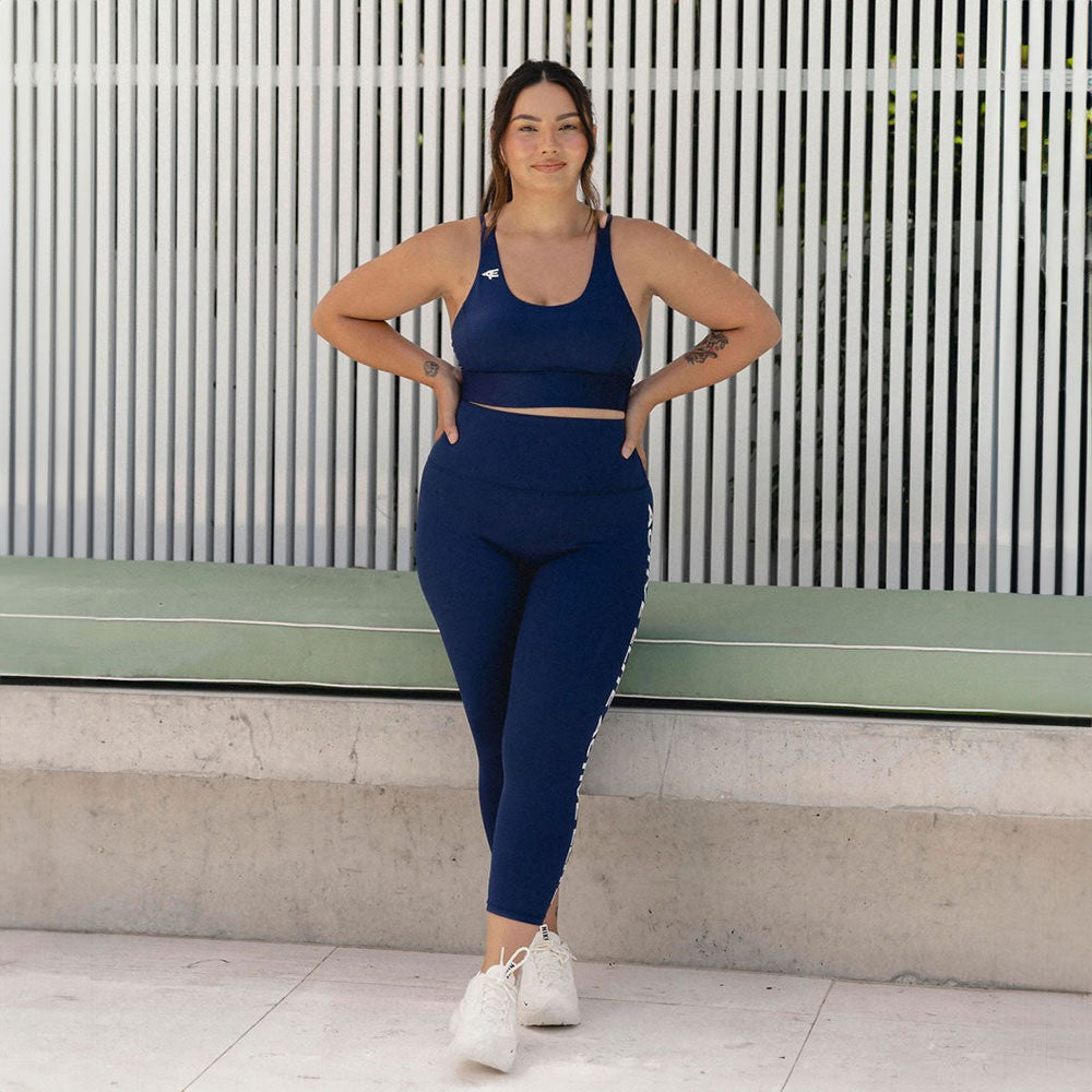 A woman confidently posing in navy activewear, emphasizing the flattering fit of the leggings and top.