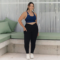 A woman standing confidently in front view, wearing a navy sports bra and black leggings, embracing body positivity and fitness.