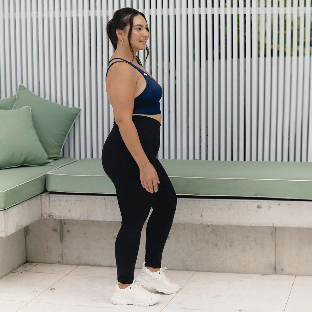 Side view of a woman showcasing the comfort and fit of navy activewear, paired with a serene background, highlighting the supportive and stylish design.