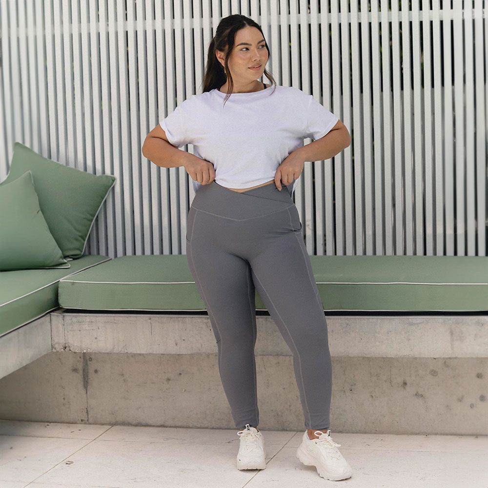 A confident woman wearing grey leggings and a white cropped tee.