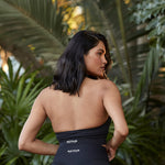 A woman confidently posing with her back facing the camera, highlighting the elegant design of the halter top by Active Elite against a lush, tropical backdrop.