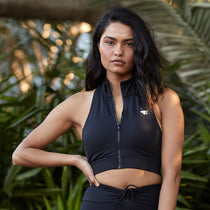 A woman posing in a black halter activewear top, exuding confidence and strength in a natural environment.