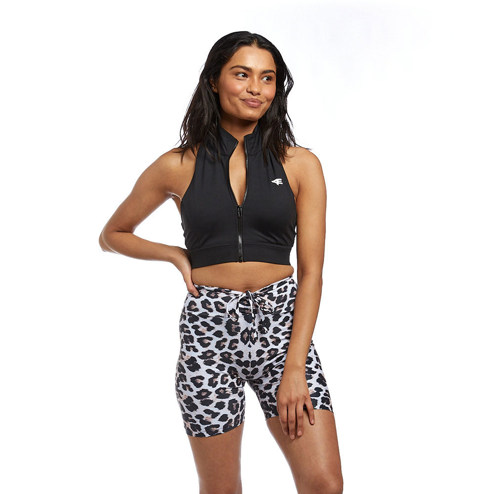 A woman in a relaxed pose, smiling, hand on hip, showcasing the black halter top and leopard print shorts. 