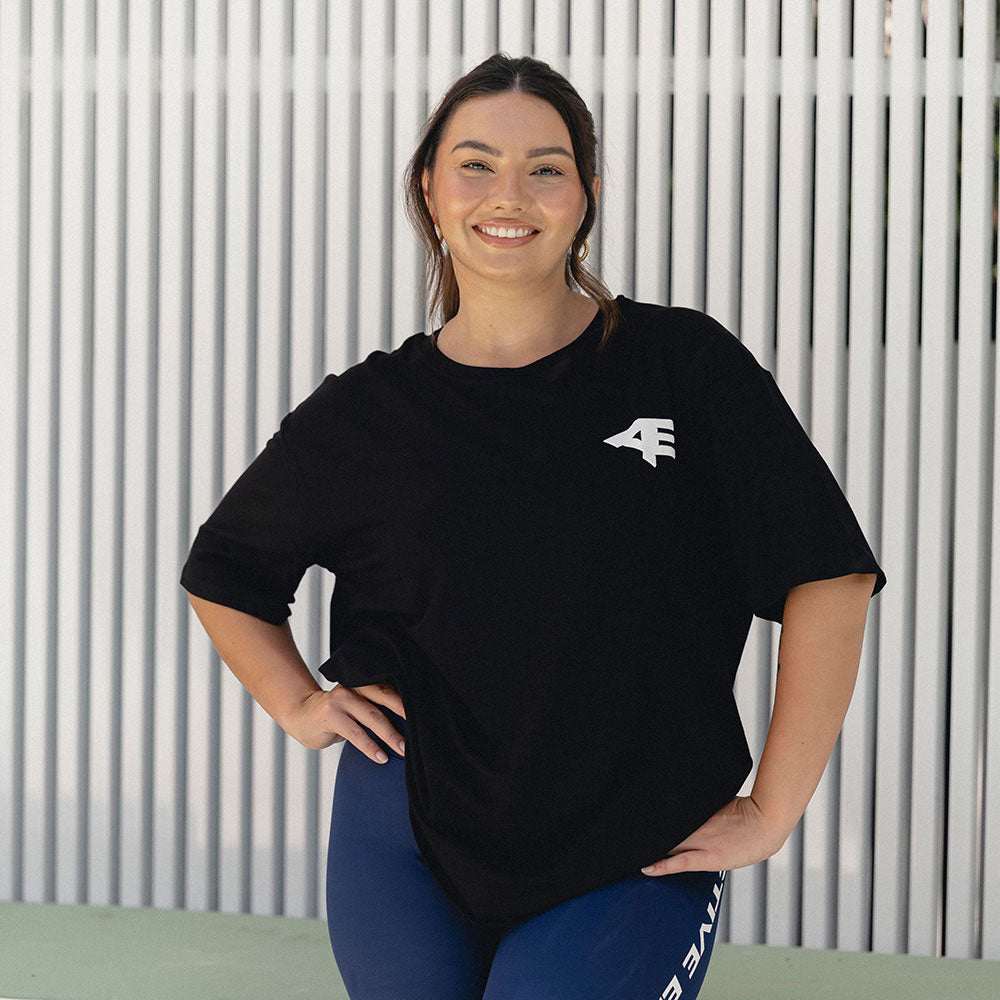 A front view of a smiling woman wearing a black oversized tee and navy leggings. She stands confidently, with her hand on her hip, exuding a relaxed yet sporty vibe in her fitness attire.