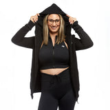 A woman playfully posing with the hood of her Active Elite black zip-up hoodie pulled over her head. She smiles broadly, combining a fun, sporty, and casual aesthetic.